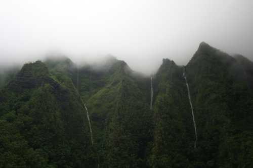 Lush green mountains shrouded in mist, with waterfalls cascading down their slopes.