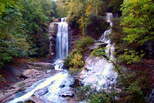 A scenic view of cascading waterfalls surrounded by lush green trees and rocky terrain.