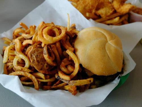 A plate of curly fries next to a hamburger on a bun, served in a paper basket.