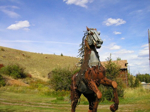 A large metal sculpture of a horse rearing up, set against a blue sky and grassy landscape.