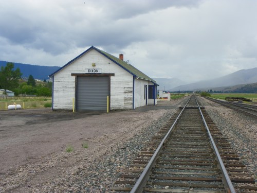 A weathered train station building labeled "Dixon" beside empty railroad tracks under a cloudy sky.