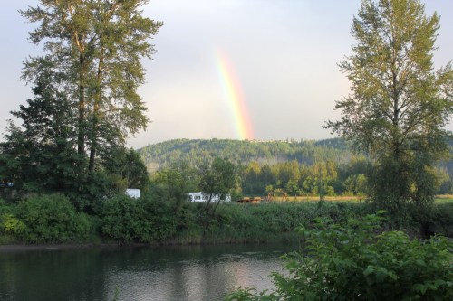 A serene landscape featuring a river, lush greenery, and a rainbow arching over a distant hill.