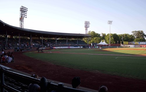 A baseball field with a grandstand, fans in the stands, and players on the field during a game at sunset.