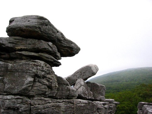 A rocky formation with large stones stacked, set against a misty green hillside.