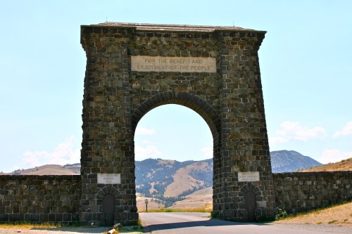 Stone archway with a sign reading "For the benefit and enjoyment of the people," set against a mountainous landscape.