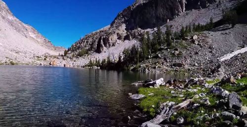 A serene mountain lake surrounded by rocky terrain and lush greenery under a clear blue sky.