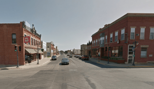 A street view of a small town intersection with brick buildings and traffic lights on a clear day.