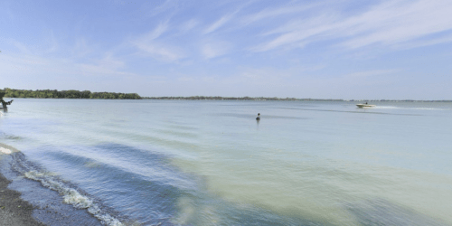 A serene lake scene with calm waters, a clear blue sky, and a boat in the distance.