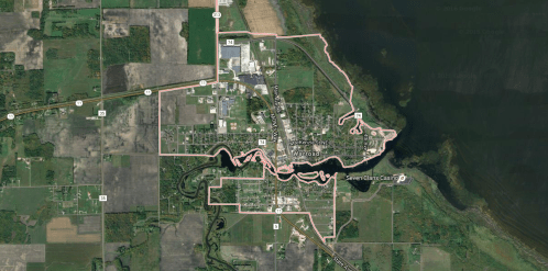Aerial map of a small town with outlined boundaries, featuring roads, water, and surrounding farmland.