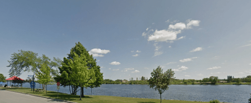 A serene lakeside view with green trees, blue sky, and fluffy clouds, featuring a calm water surface.