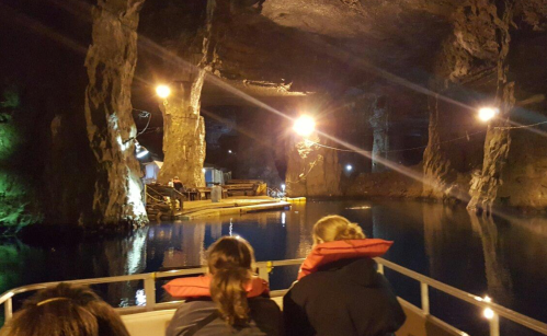 A boat ride inside a dimly lit cave, with reflections on the water and illuminated rock formations.