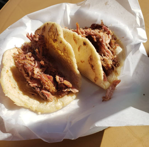 Three tacos filled with shredded meat, served on a white paper plate.