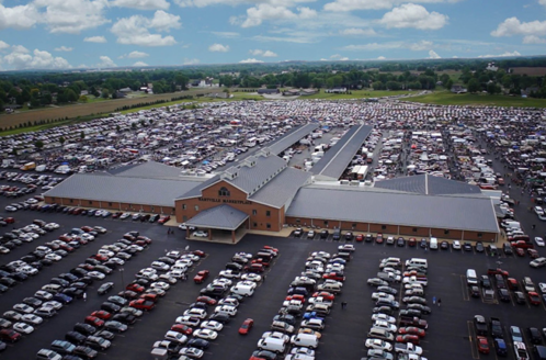 Aerial view of a large parking lot filled with cars, adjacent to a spacious building under a blue sky with clouds.