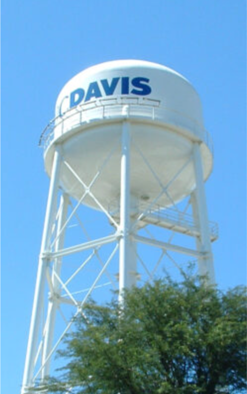 White water tower with "DAVIS" written in blue, set against a clear blue sky and surrounded by green foliage.