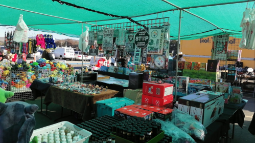 A vibrant outdoor market stall filled with various merchandise, including toys, crafts, and household items under a green canopy.