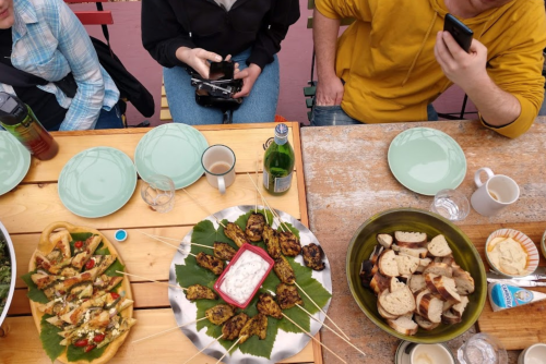 A table set with various dishes, including skewers, bread, and drinks, with people seated around it.