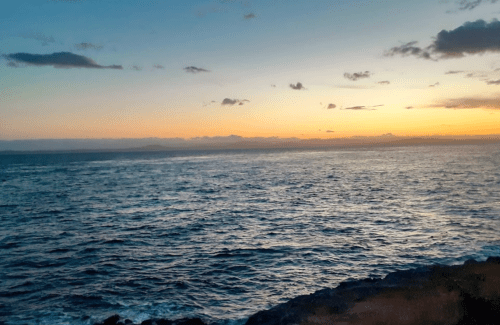 A serene ocean view at sunset, with gentle waves and a colorful sky filled with clouds.
