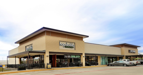 Exterior view of a Hopdoddy Burger Bar restaurant, featuring a modern design and a "Now Open" sign.