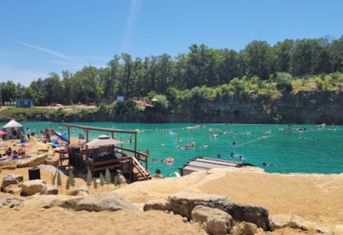 A sunny day at a swimming area with people in the water, surrounded by trees and a wooden dock.