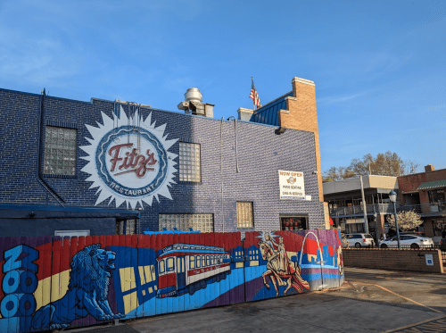A blue building with a mural featuring a lion and a streetcar, advertising "Fitz's Restaurant" and "Now Open."