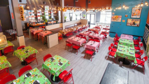 A vibrant restaurant interior with red chairs and colorful tables, featuring tropical tablecloths and warm lighting.