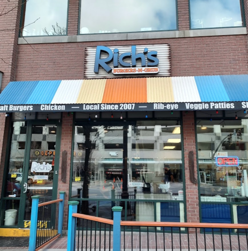 Exterior of Rich's Burgers-N-Grill, featuring a colorful awning and large windows, with an "Open" sign visible.