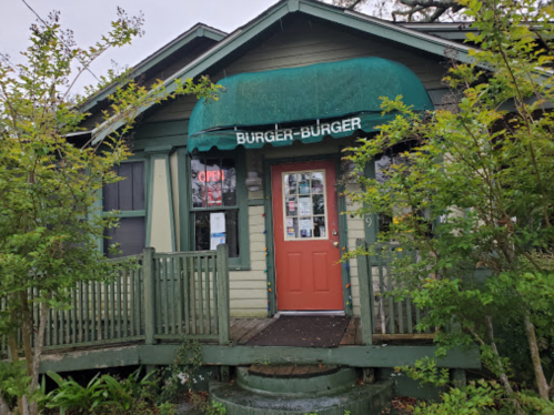 A green house with a sign reading "Burger-Burger" and an open sign, surrounded by greenery.