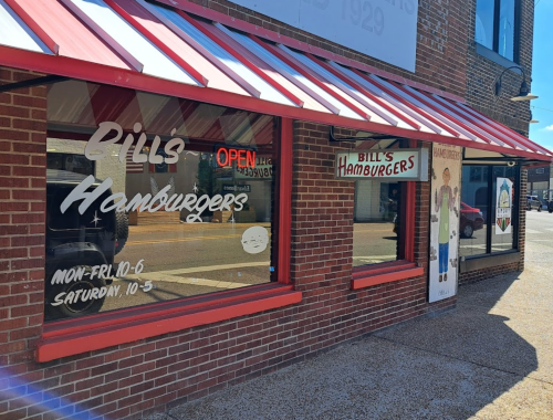 Exterior of Bill's Hamburgers with a red and white awning, featuring hours and a sign indicating it's open.