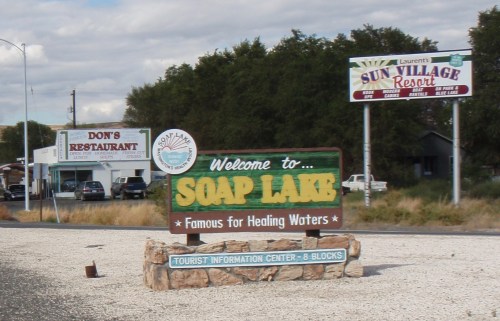 Welcome sign for Soap Lake, highlighting its famous healing waters, with nearby restaurant and resort advertisements.