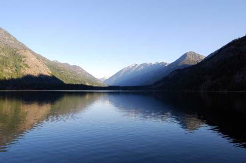 A serene lake surrounded by mountains, reflecting the clear blue sky and lush greenery on the water's surface.