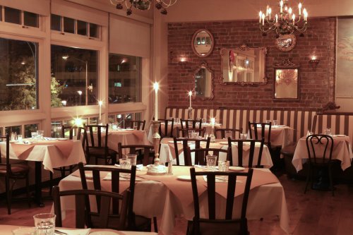 Cozy restaurant interior with wooden chairs, tables set with white tablecloths, and warm lighting from chandeliers.