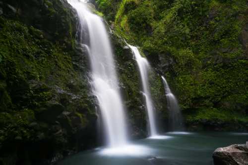 A serene waterfall cascading down rocky cliffs, surrounded by lush green foliage and a tranquil pool below.