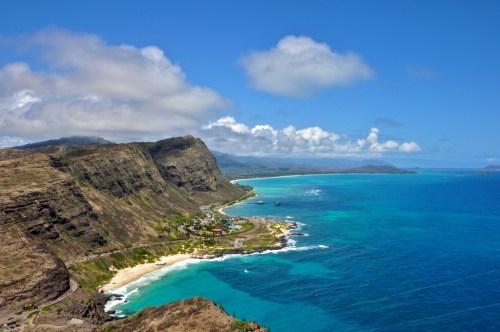 A scenic coastal view featuring cliffs, turquoise waters, and a sandy beach under a blue sky with scattered clouds.