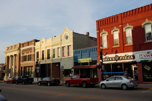 A street view featuring historic buildings and shops, including a pizza place, under a clear sky.