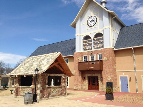 A building with a clock tower, featuring a stone and wood gazebo in the foreground and a clear blue sky.