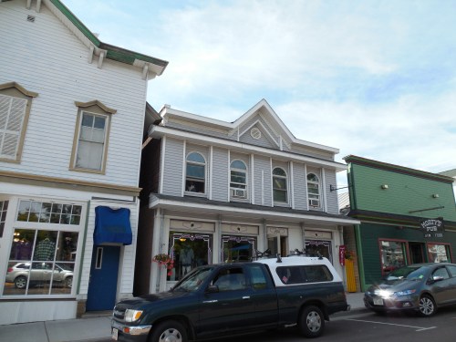 A quaint street scene featuring a two-story building with decorative windows and nearby shops, under a cloudy sky.