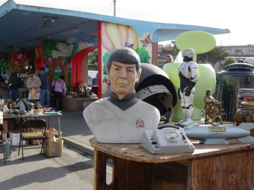 A Spock bust on a table at a vibrant outdoor market, with various collectibles and people browsing in the background.