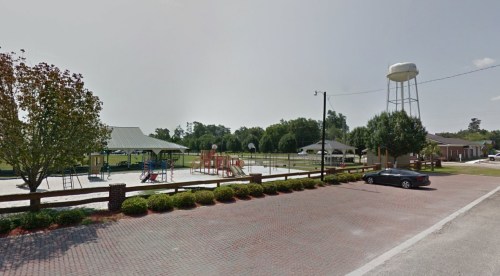 A playground with equipment, a basketball court, and a water tower in a green park setting.