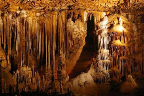 Stalactites and stalagmites in a dimly lit cave, showcasing intricate rock formations and textures.