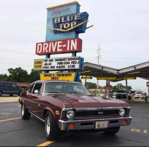 A classic maroon car parked in front of a retro drive-in sign for Johnson's Blue Top Drive-In.