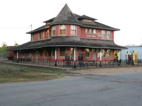 Historic train station with a distinctive turret, featuring red siding and a wraparound porch.