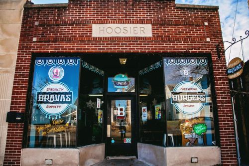 Exterior of Bravas Burgers restaurant, featuring a brick facade and large windows with colorful signage in Fort Wayne, Indiana.
