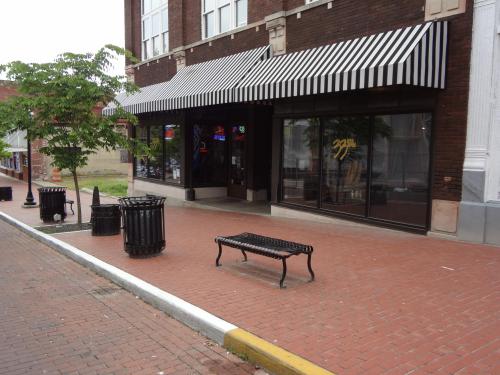 A brick sidewalk with a bench, trash cans, and a storefront featuring striped awnings and large windows.