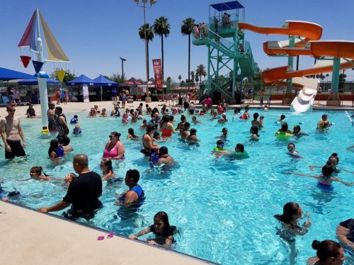 A crowded pool scene with people swimming and enjoying water slides under a clear blue sky.