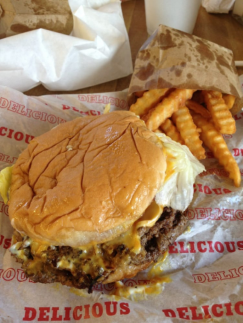 A juicy cheeseburger with lettuce on a bun, accompanied by crispy waffle fries on a red and white paper.