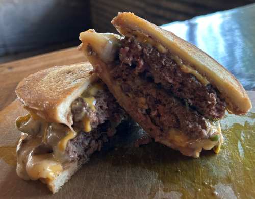 A close-up of a juicy burger with melted cheese, served on toasted bread, cut in half to reveal its layers.