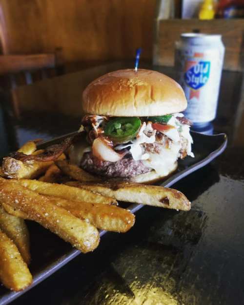 A juicy burger topped with jalapeños and coleslaw, served with crispy fries and a can of Old Style beer.