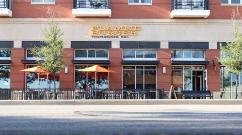 Exterior of Flamme Burger restaurant with orange umbrellas and a modern brick facade.