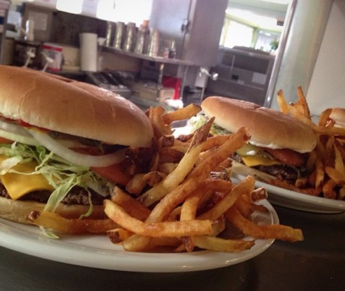 Two burgers with lettuce, tomato, onions, and cheese, served with a side of golden French fries on white plates.