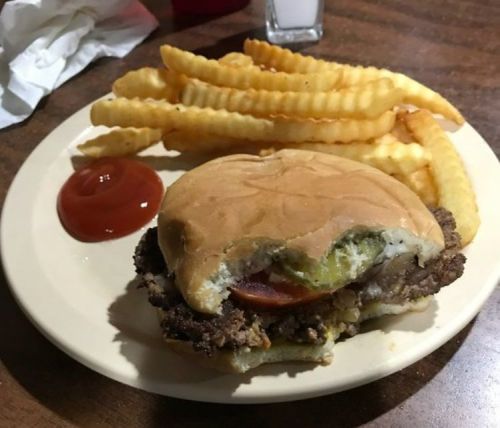 A plate with a half-eaten burger topped with pickles and a side of crinkle-cut fries and ketchup.